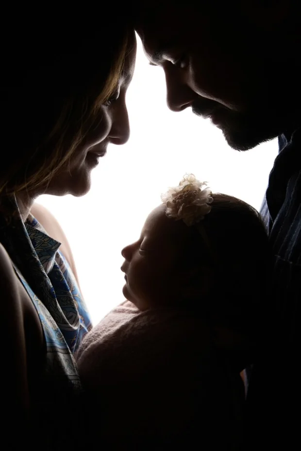 Nivisha, held between her parents, in silhouette against a window of light